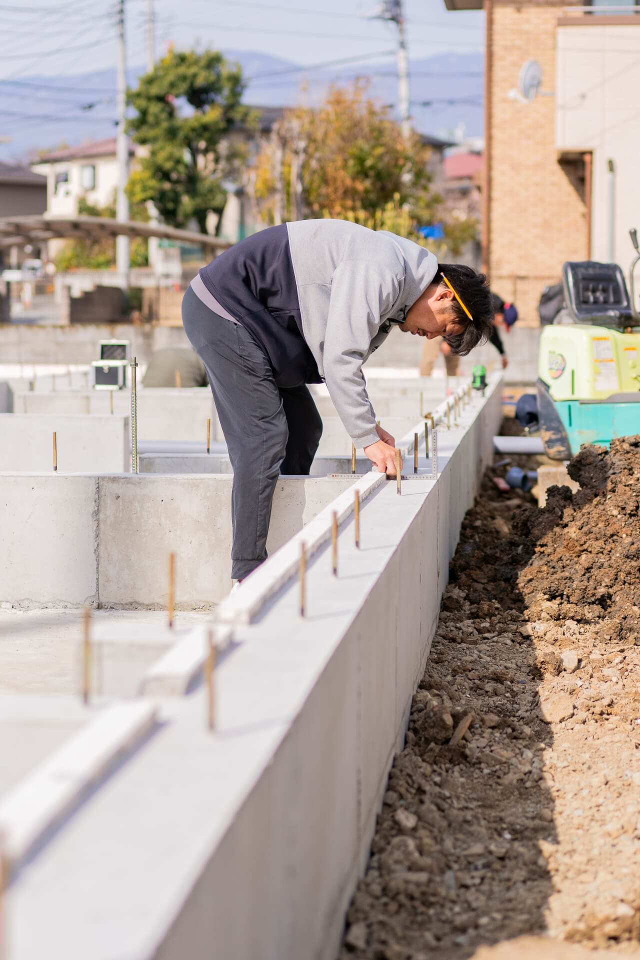 山梨県の住宅基礎工事現場で、丁張の確認作業を行う現場監督。土台敷きに向けた精密な測定を実施している様子。