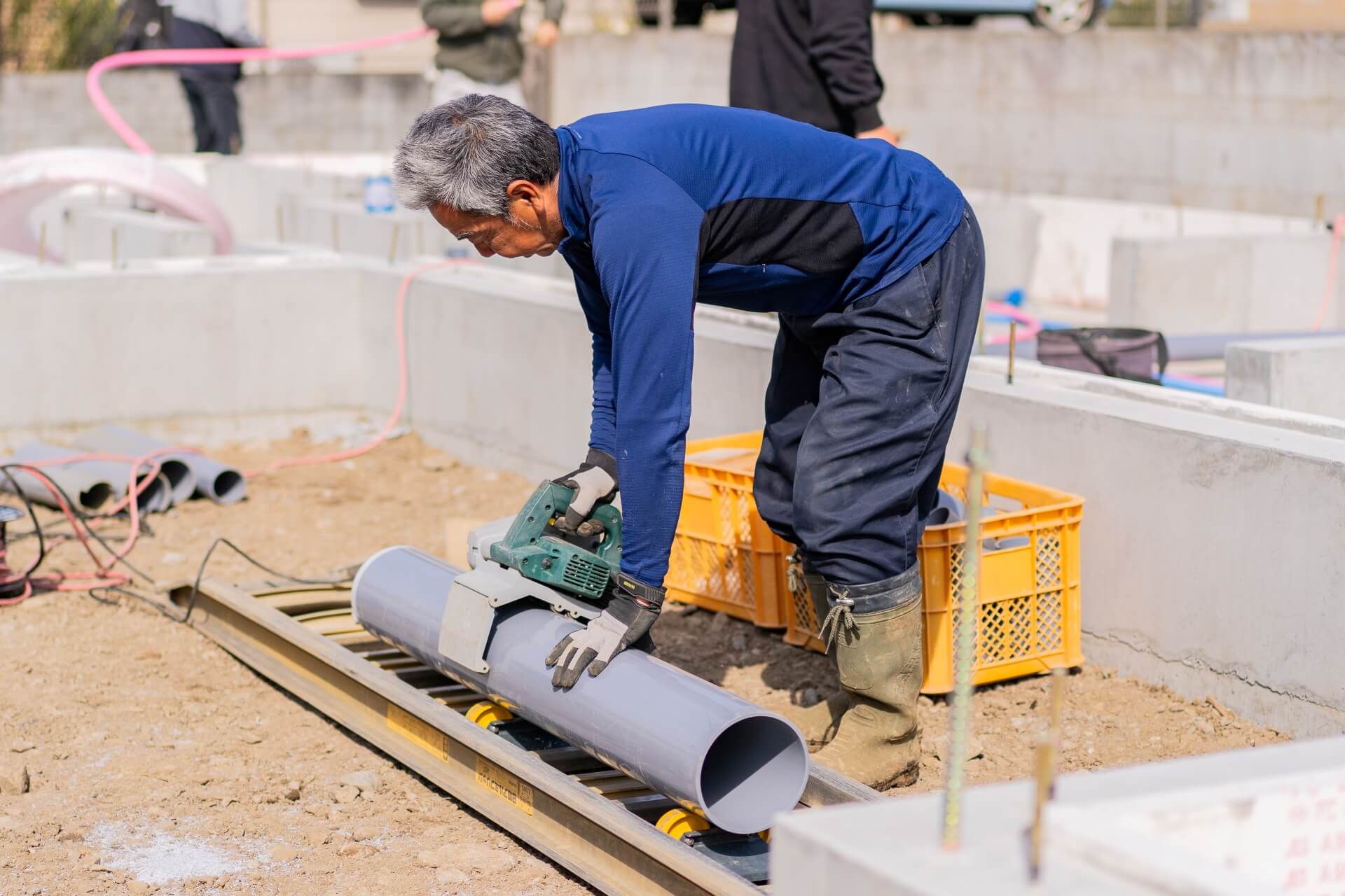 住宅基礎工事現場で配管を電動工具でカットしている職人の作業風景。丁寧な調整が進められている様子。