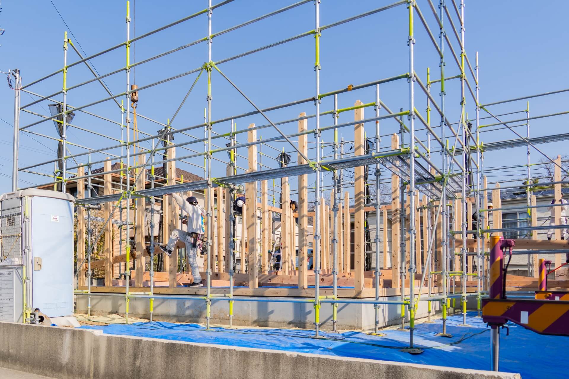 山梨県の住宅現場で、柱の建て込み作業を進める職人の様子。足場が組まれ、家の骨組みが着実に立ち上がっていく光景。