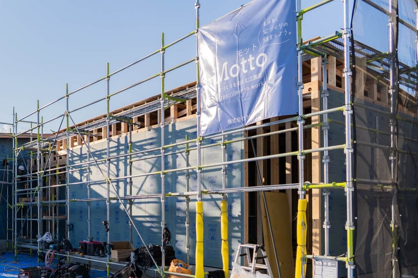 山梨県の住宅現場で、外周部の体力面材が施工されている様子。足場にはMottoの工事幕が掲げられている。