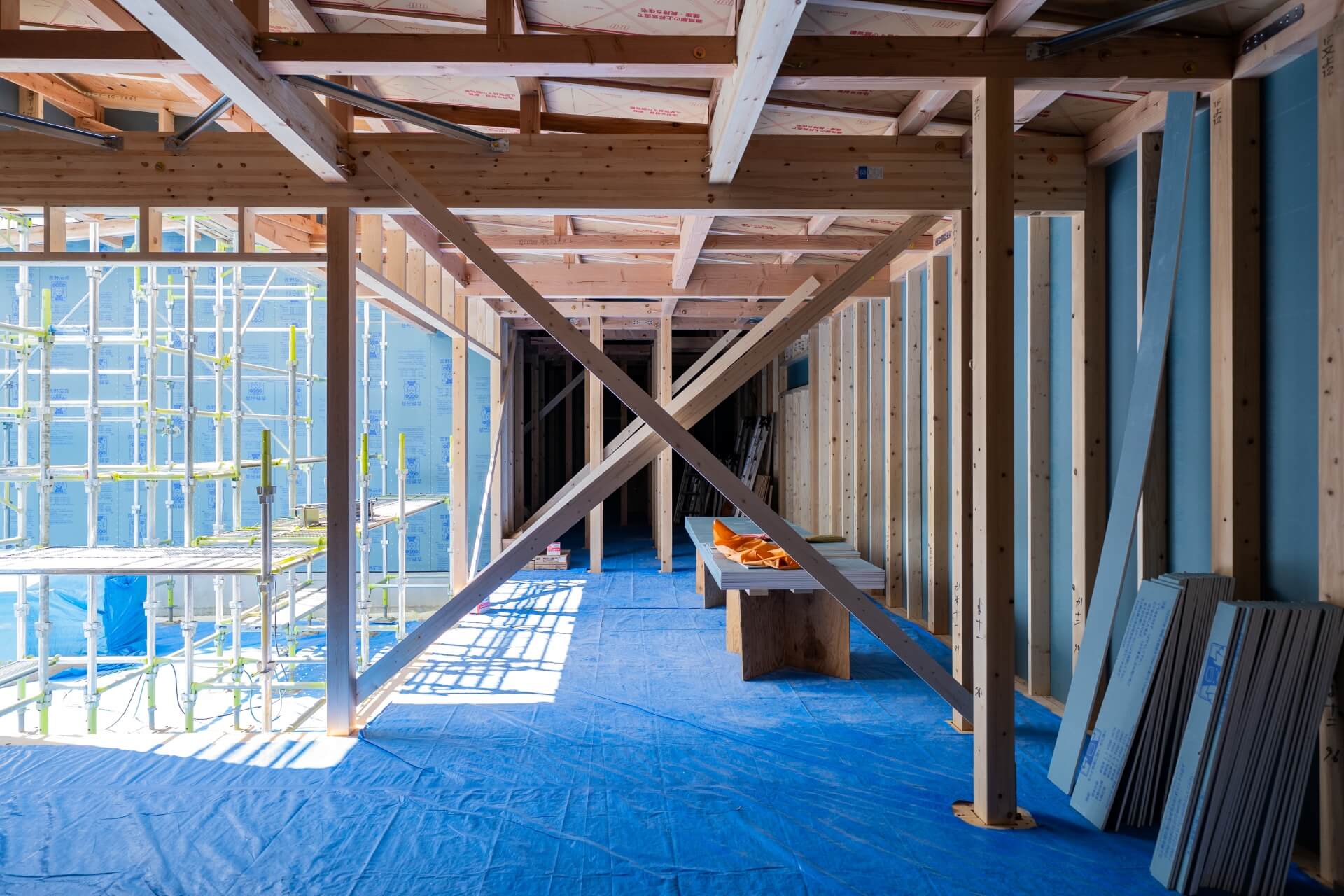 山梨県の住宅建築現場で、LDKと中庭部分の様子が見える状態。木造の柱と梁、青い養生シートが敷かれている。