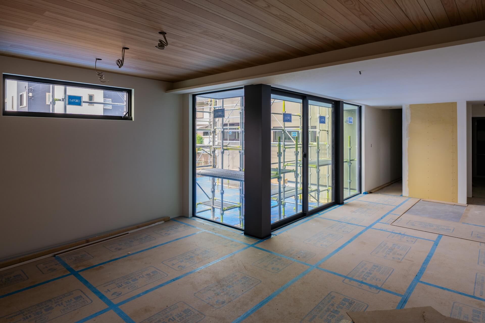 山梨県甲斐市竜王新町の建築現場で床に養生された室内の様子。天井には木目材を使用