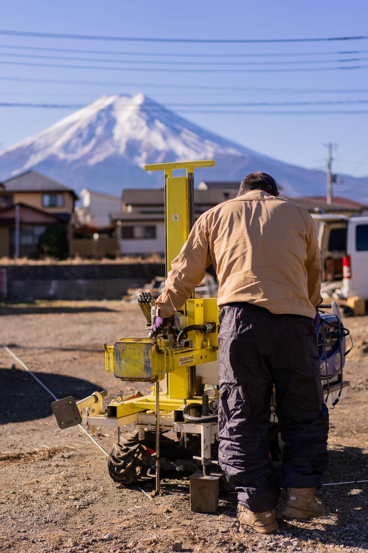 山梨県富士吉田市大明見の建築現場。地盤調査の様子。富士山を背景に、住宅建築に向けて地盤の状態を確認している場面。