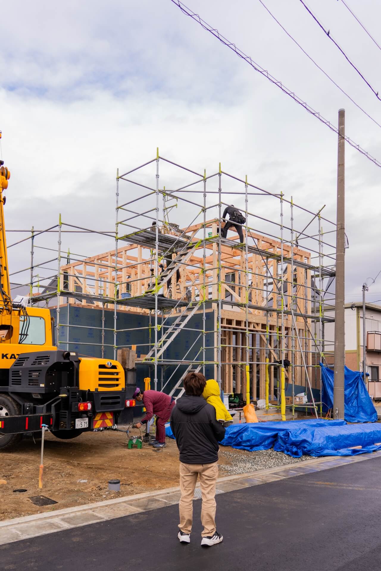 山梨県甲府市蓬沢の新築現場にて上棟工事の様子を見守るご家族の後ろ姿。