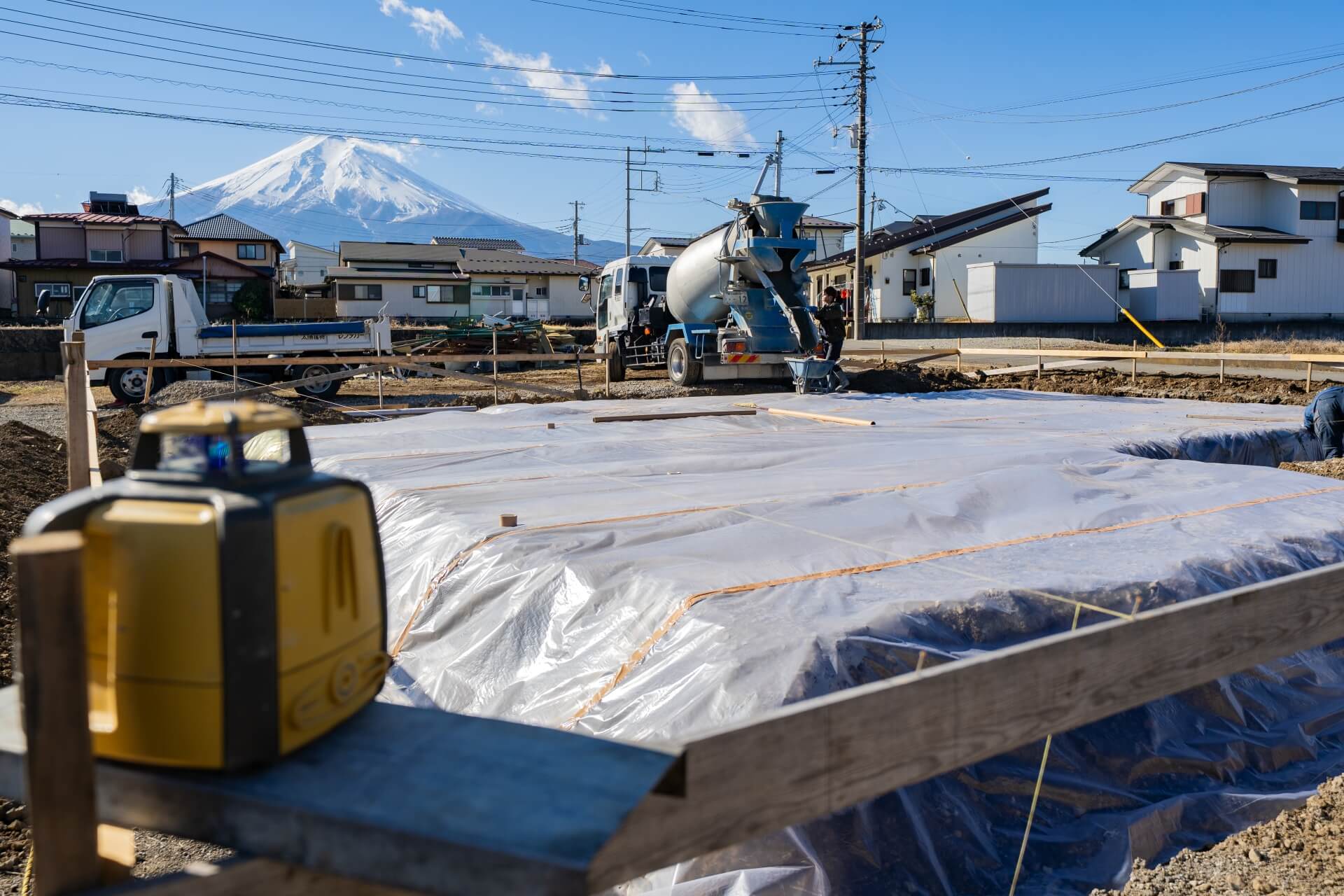 山梨県富士吉田市大明見の建築現場。防湿シートが敷かれた基礎工事中の現場。手前には測量機器が置かれ、正確な施工が行われている様子。