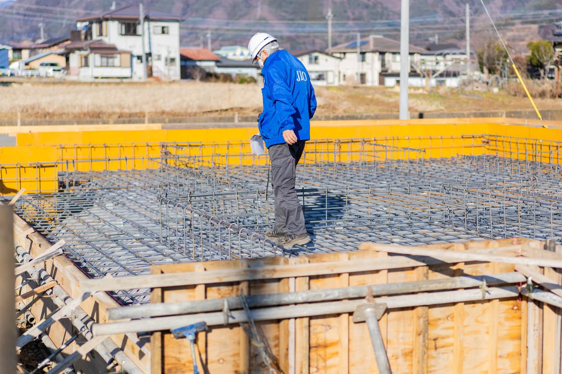 山梨県富士吉田市大明見の建築現場。基礎の配筋が組まれた状態で、設計士がチェックを行う様子。施工精度を細かくチェックしている工程。