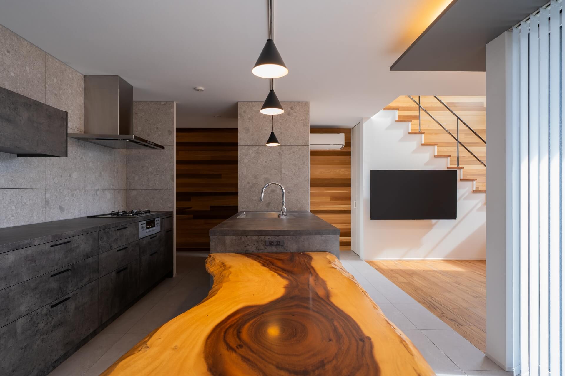 山梨県南アルプス市寺部の新築現場、グレー基調のキッチンに対して、耳付きの一枚板カウンターがアクセントになるダイニング空間。