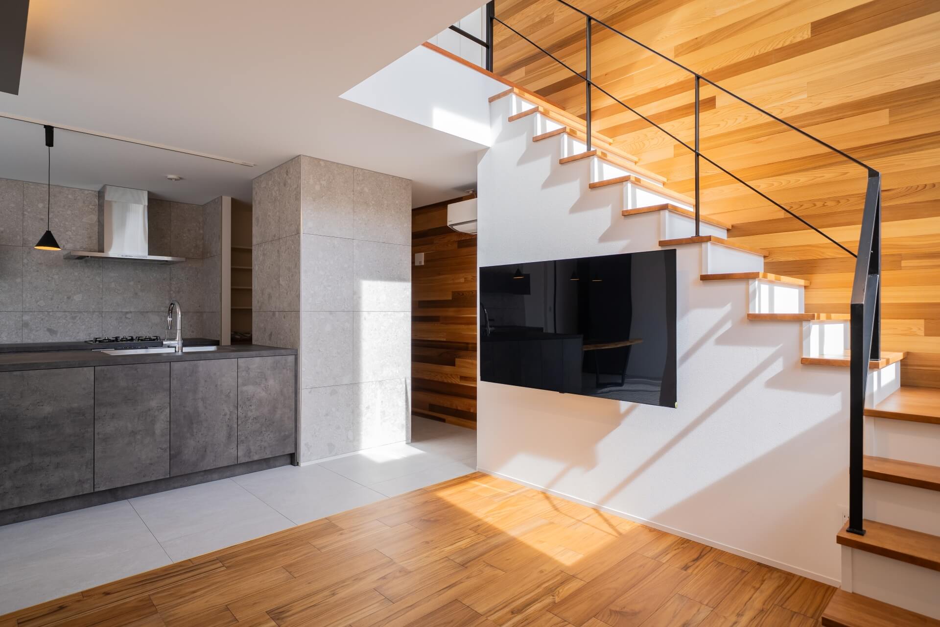 山梨県南アルプス市寺部の新築現場、スケルトン階段と白い壁面に設置されたテレビ。自然光が差し込み陰影が美しいリビング。