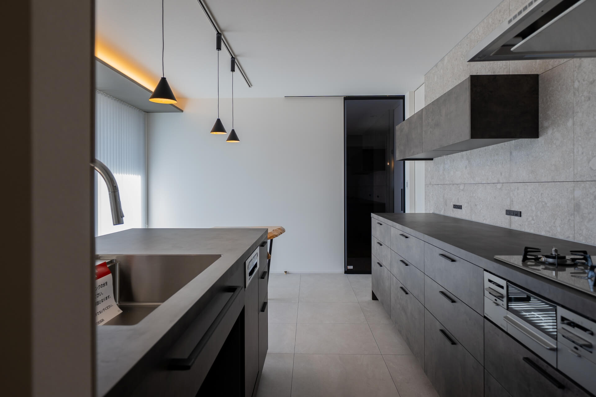 山梨県南アルプス市寺部の新築現場、アイランドキッチンから奥へ視線が抜けるレイアウト。ペンダント照明と一直線の動線が美しい。