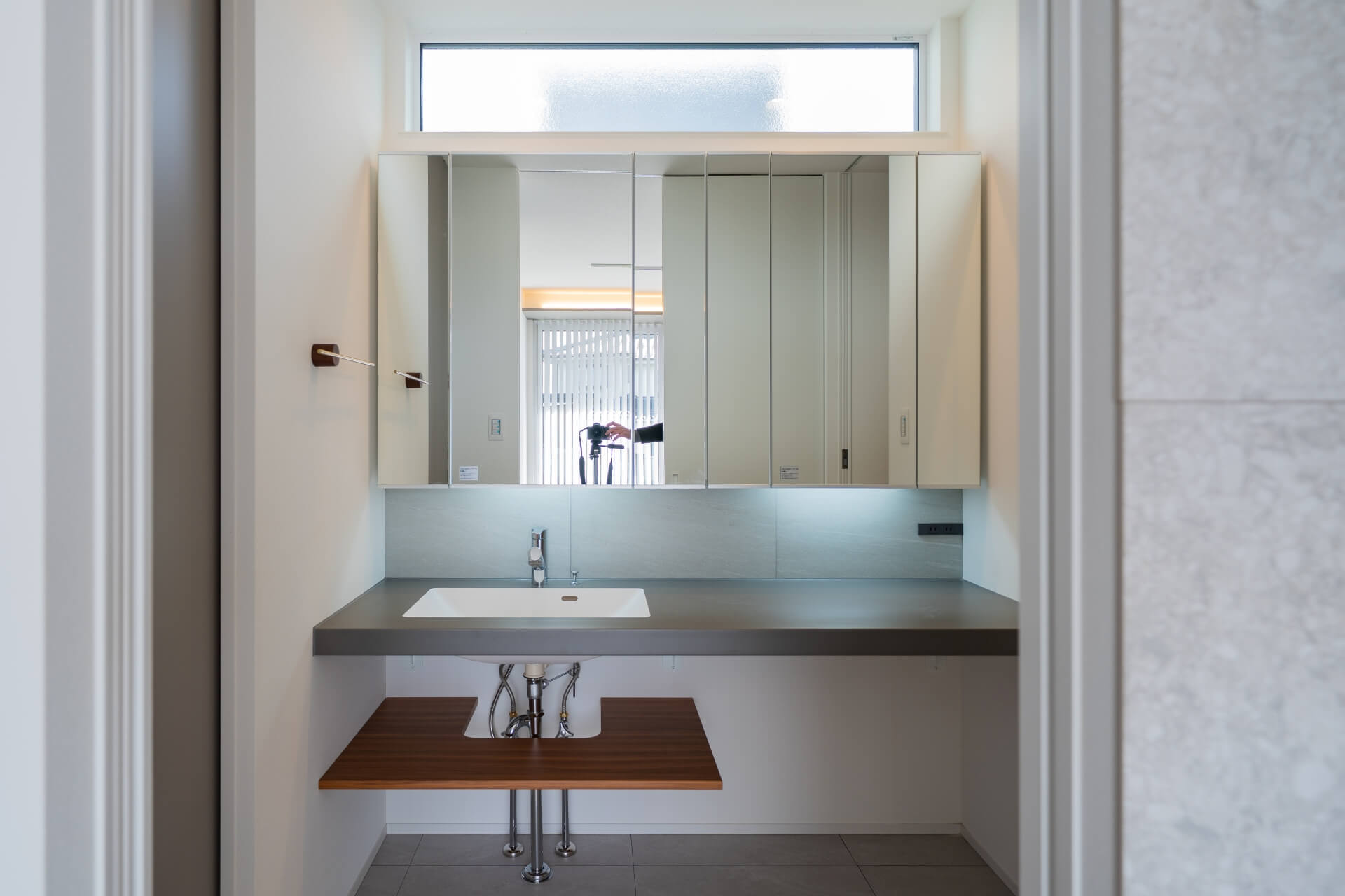 山梨県南アルプス市寺部の新築現場、三面鏡収納で生活用品を隠し、カウンターと木の棚でバランスを取った洗面スペース。