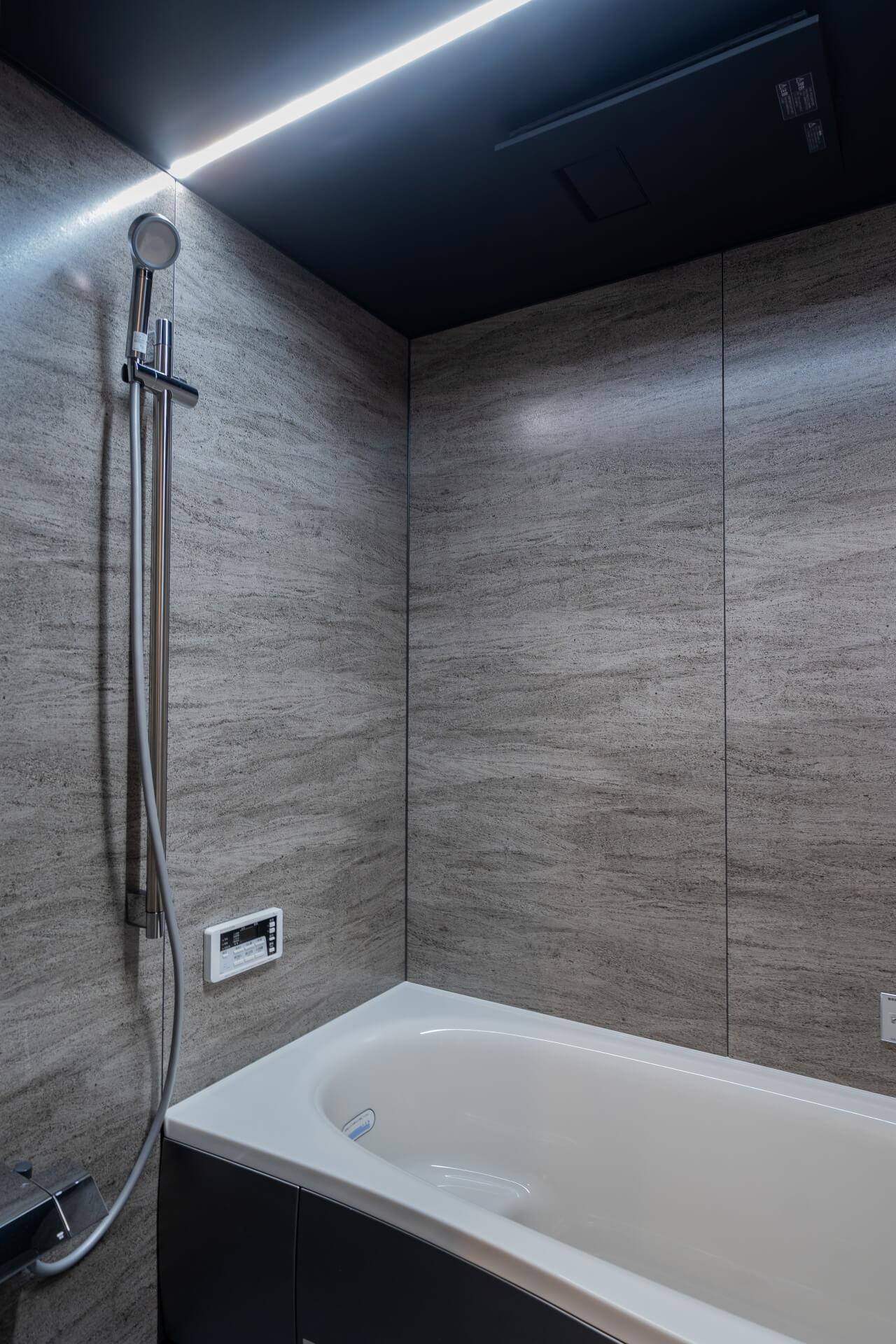 山梨県南アルプス市寺部の新築現場、石調パネルとブラック天井で構成されたシックな浴室。間接照明が空間に奥行きを与える。