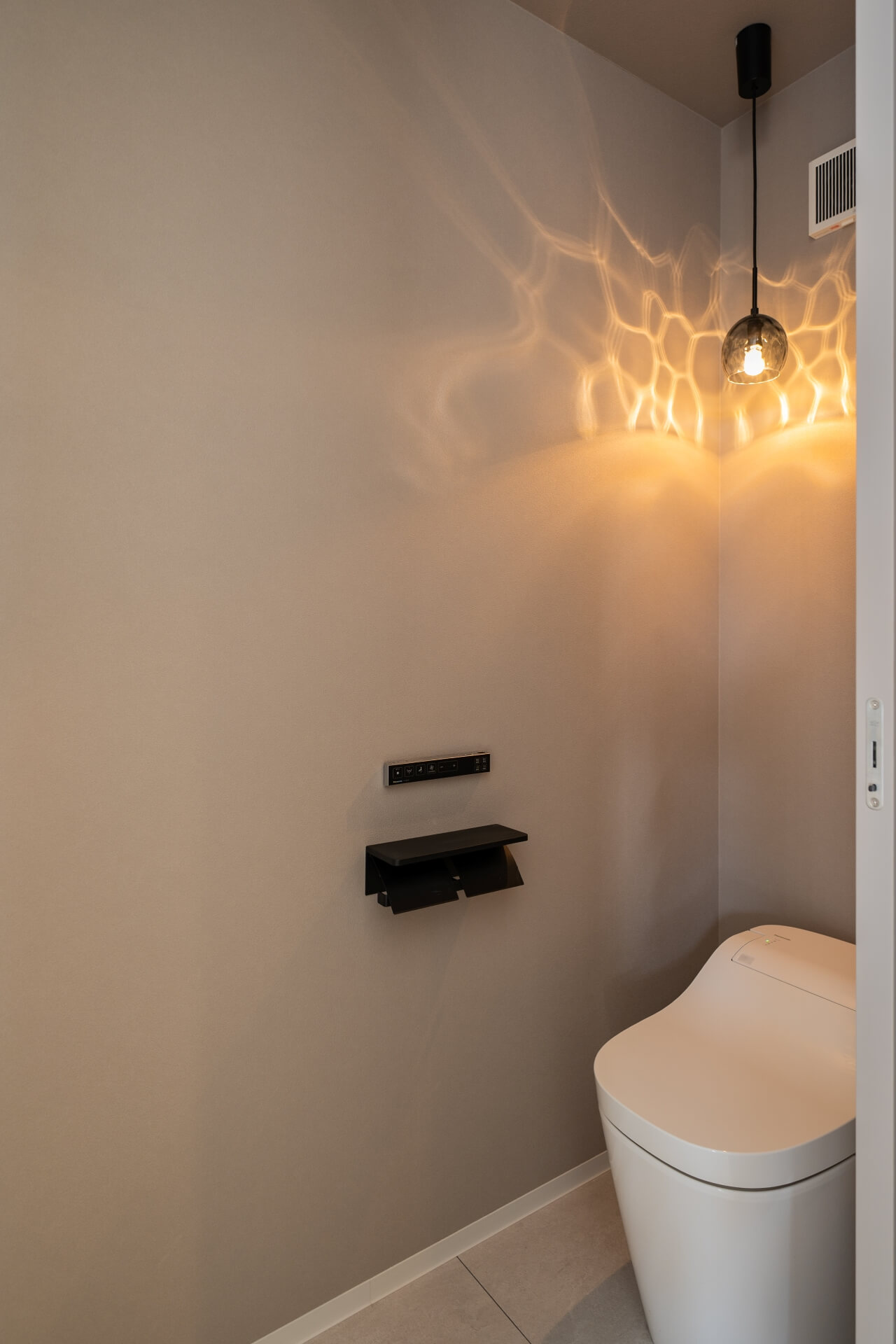 山梨県南アルプス市寺部の新築現場、ペンダント照明の反射で壁に揺らぎが生まれるトイレ空間。シンプルな設備との対比が美しい。