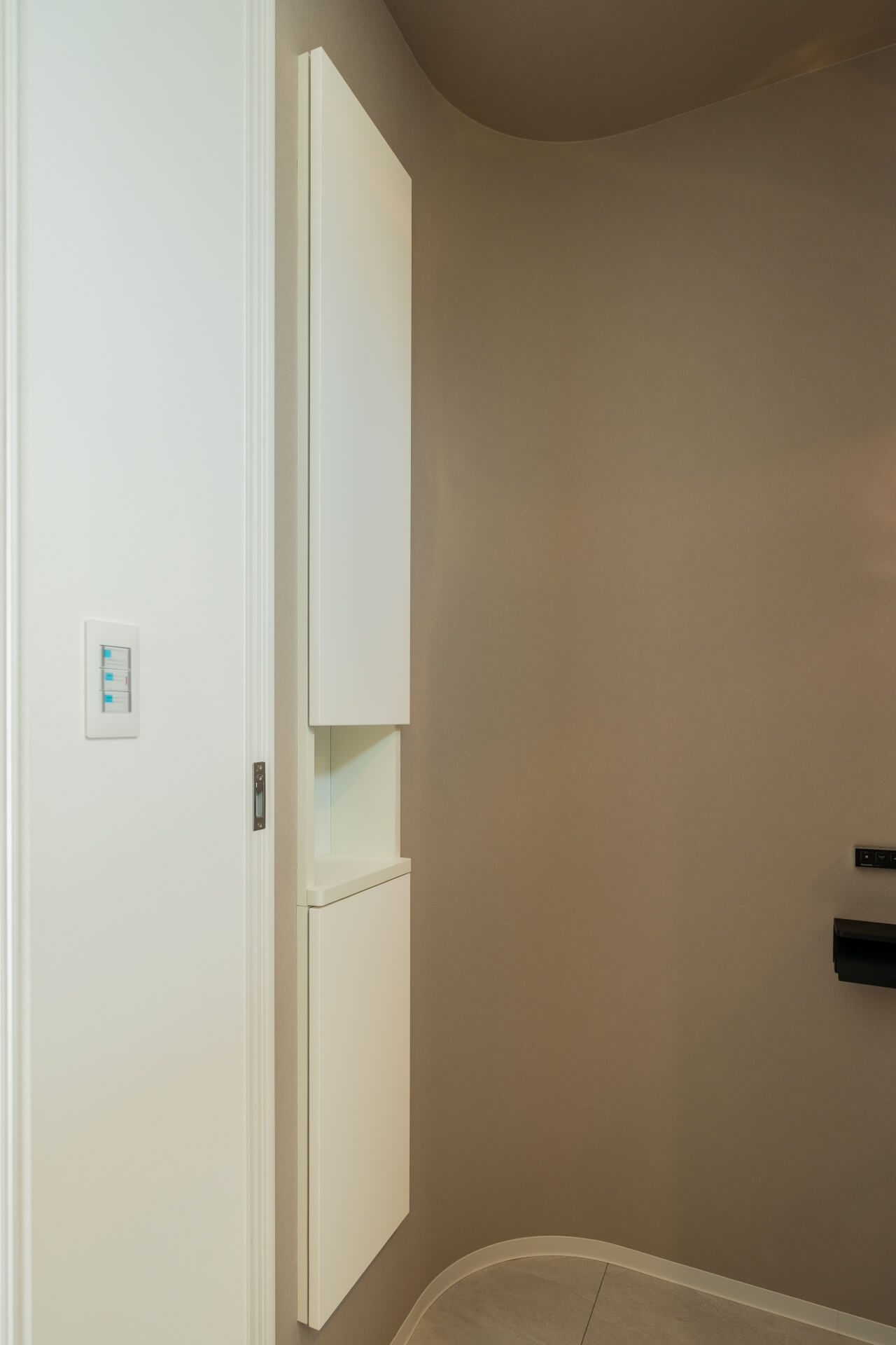 山梨県南アルプス市寺部の新築現場、曲面の壁とグレージュのクロスで構成されたトイレ入口。白い収納がすっきりと納まる。