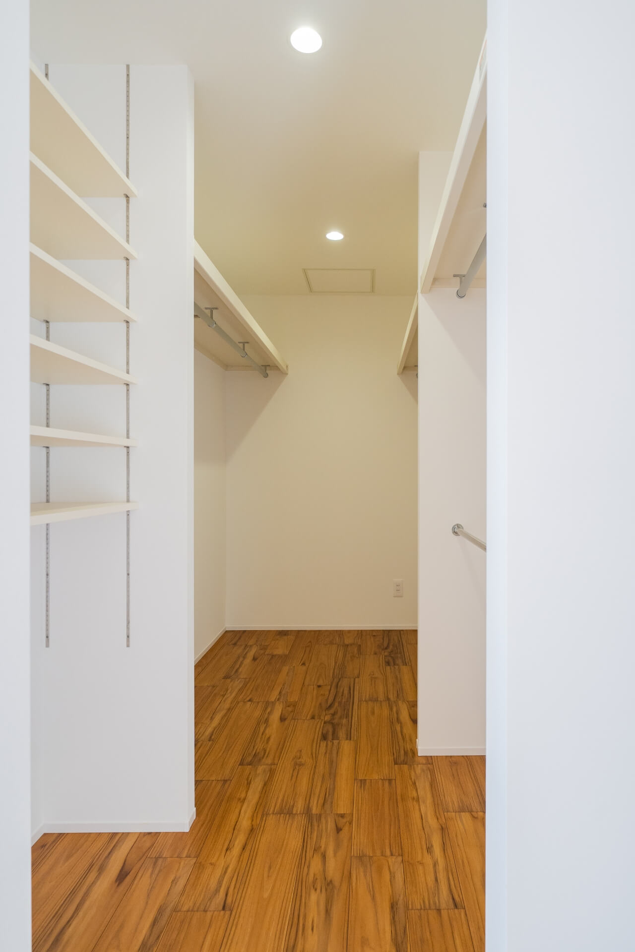 山梨県南アルプス市寺部の新築現場、両側にハンガーパイプと可動棚を設けたウォークインクローゼット。通路幅にゆとりがあり、出し入れしやすい設計。