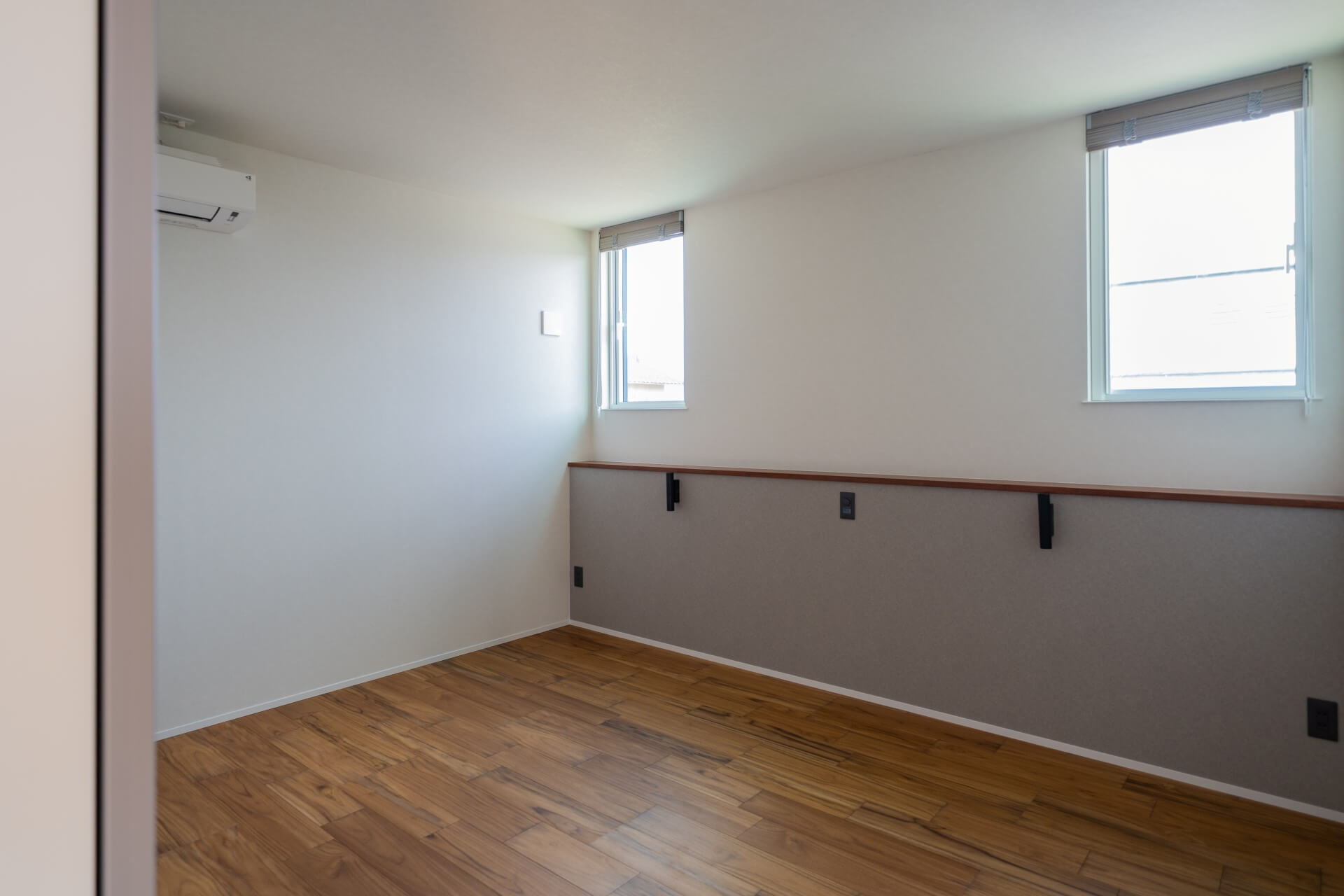 山梨県南アルプス市寺部の新築現場、2つの窓から自然光が入る洋室。木目の床とシンプルな壁で落ち着いた空間。