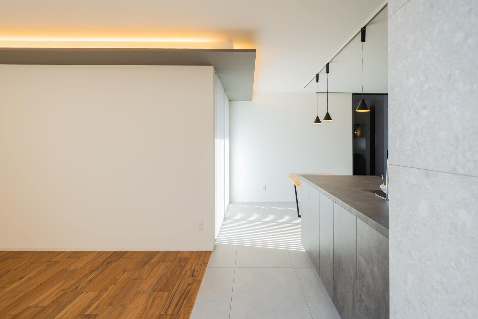 山梨県南アルプス市寺部の新築現場、キッチン横から見たLDK。間接照明と自然光が重なり、奥行きのある空間をつくる。