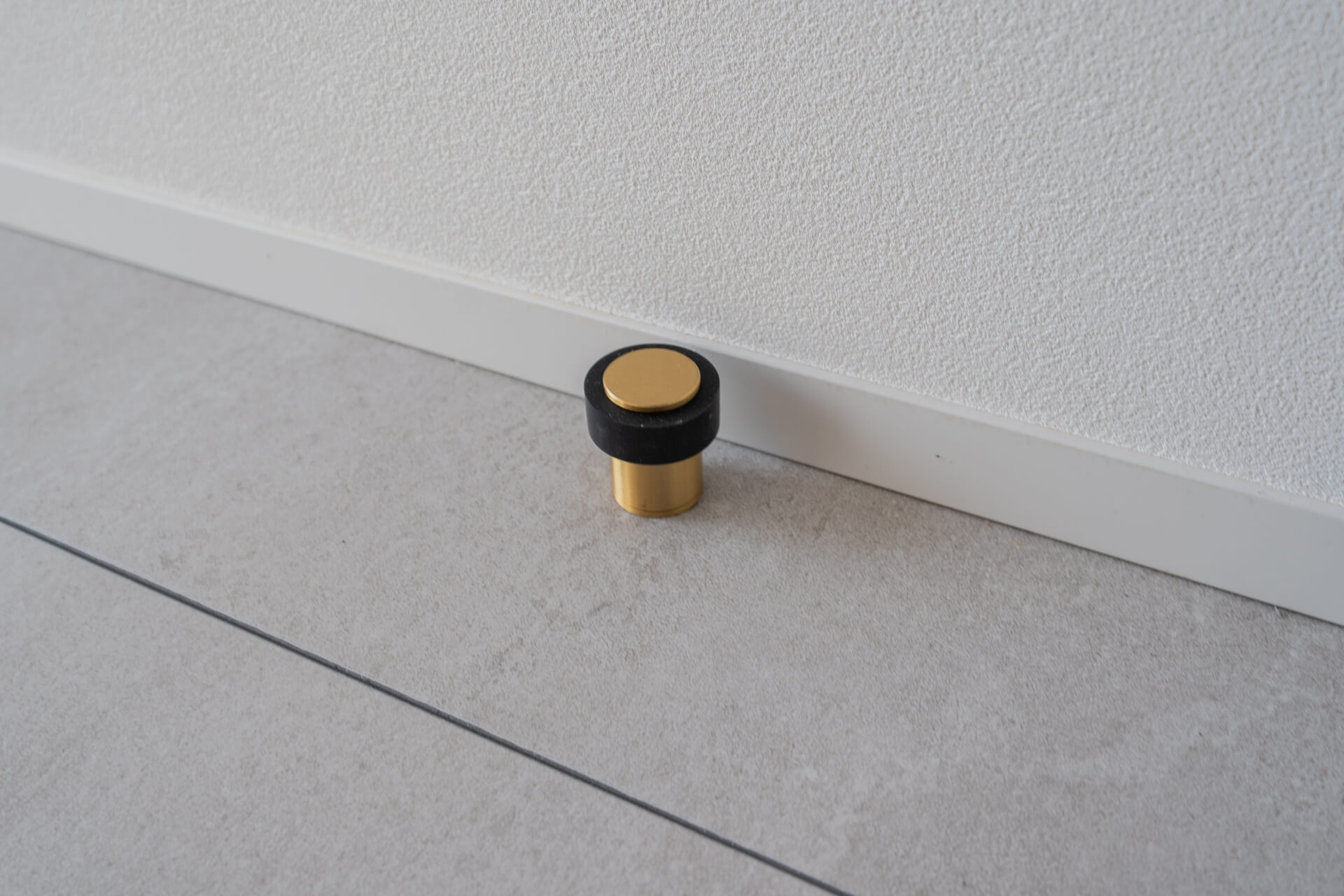 山梨県南アルプス市寺部の新築現場、真鍮と黒いゴムで構成された床付けのドアストッパー。シンプルで上質な金物ディテール。