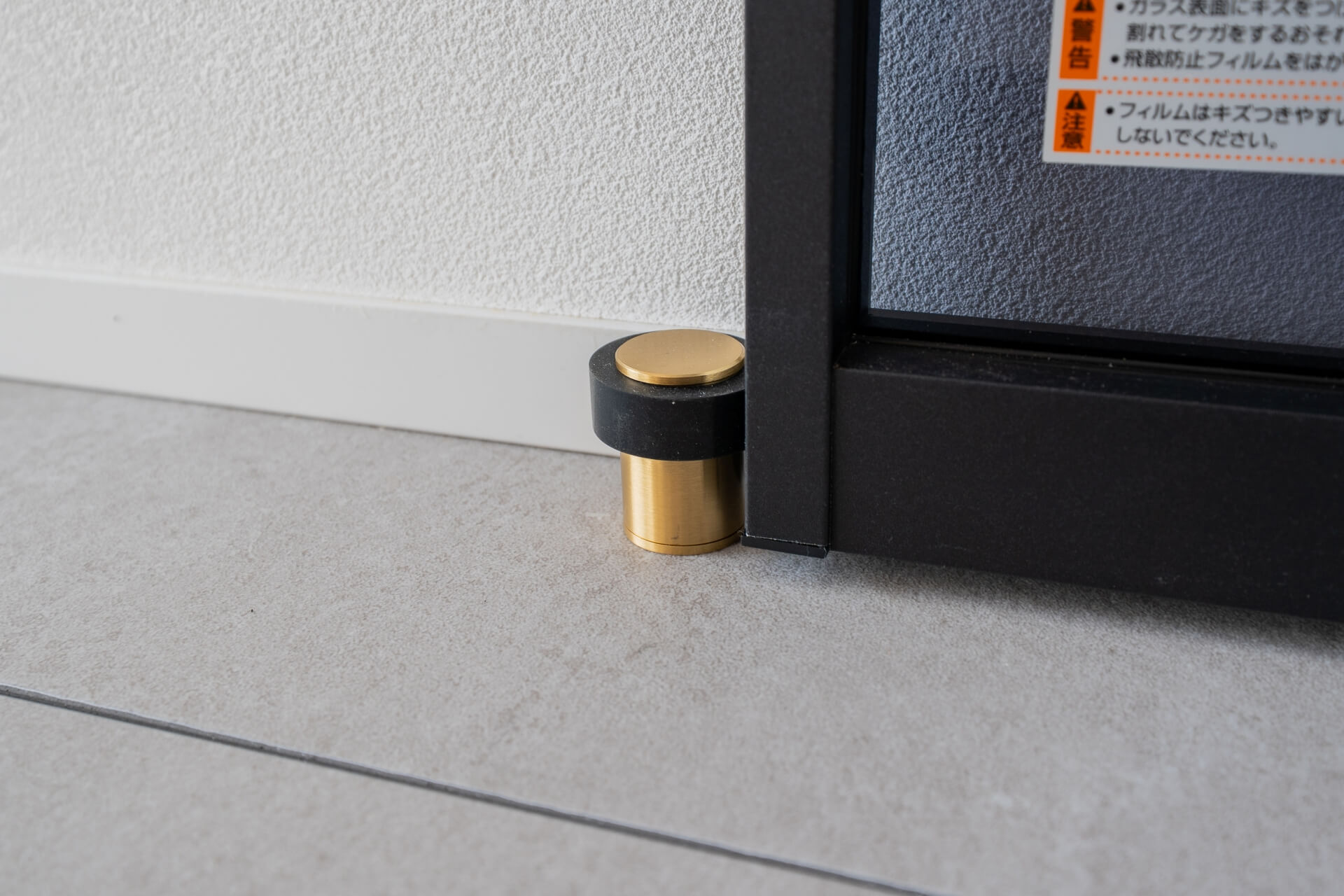 山梨県南アルプス市寺部の新築現場、真鍮とブラックのドアストッパーがガラスドアを受け止めるディテール。床タイルと建具の納まりが美しい。