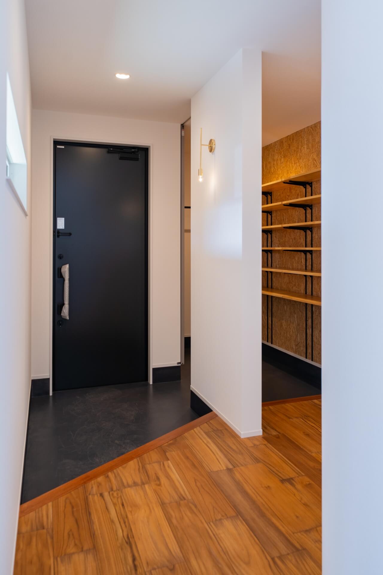 山梨県南アルプス市寺部の新築現場、黒い玄関ドアと土間、隣にシューズクロークへ続く動線がある玄関空間。