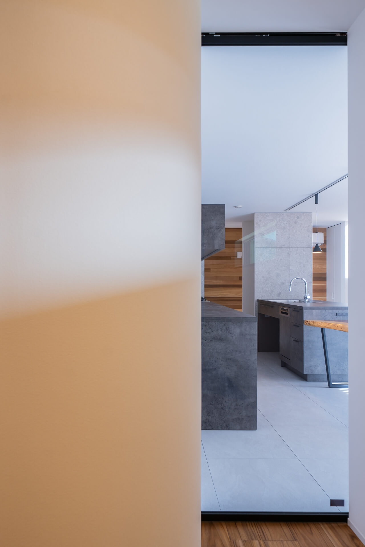 山梨県南アルプス市寺部の新築現場、玄関ホールから見たキッチン方向。グレーのキッチンと木の壁が印象的なLDK空間。