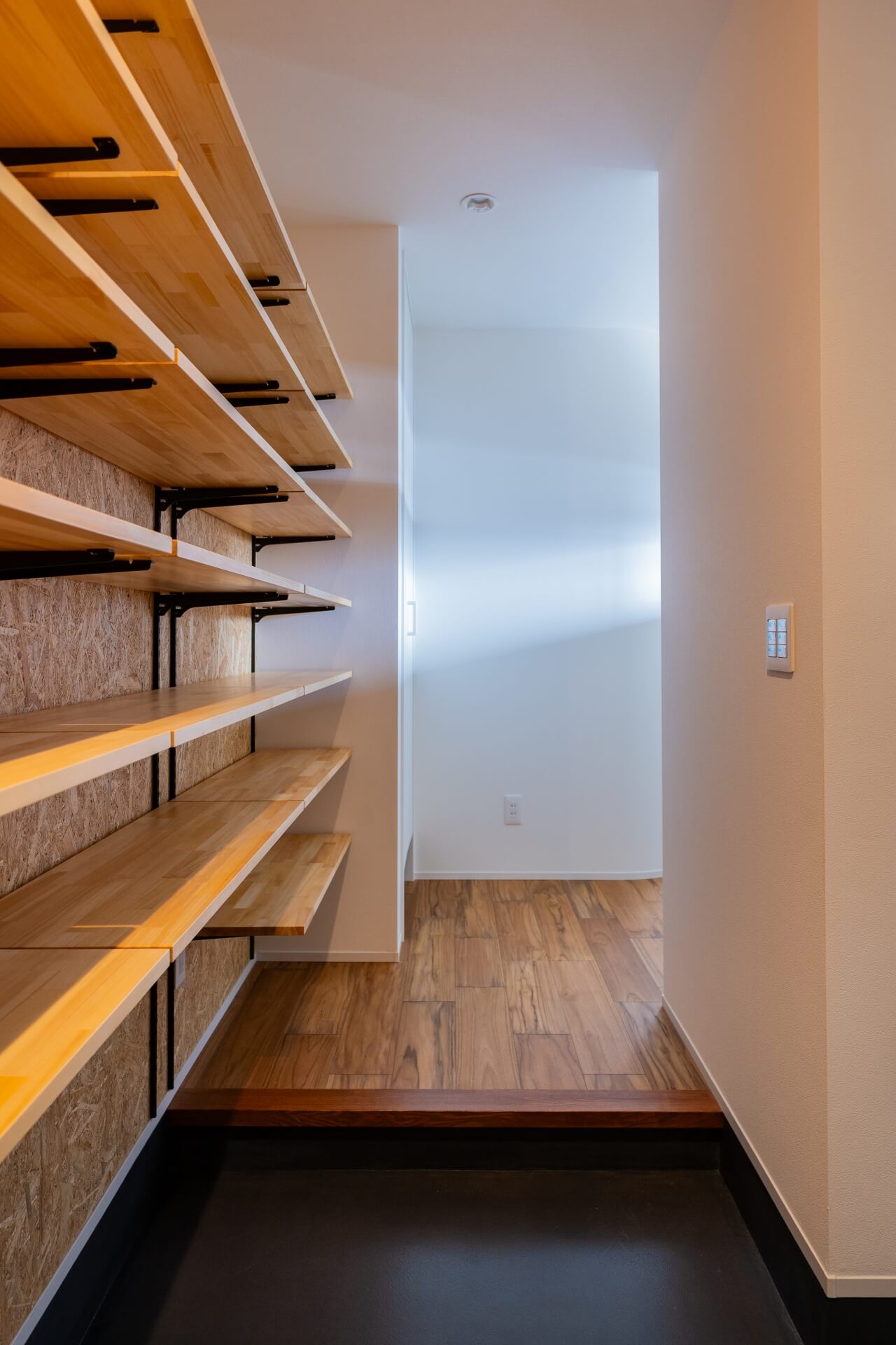 山梨県南アルプス市寺部の新築現場、可動棚が並ぶシューズクローク。木の棚板と黒い金物、OSBボードの壁が特徴的な収納空間。