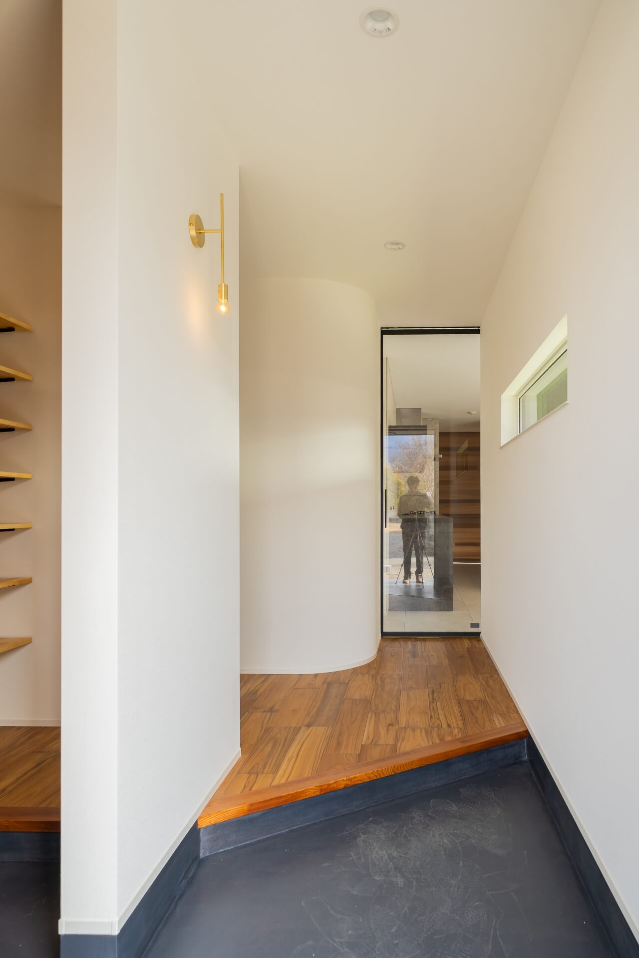 山梨県南アルプス市寺部の新築現場、曲面の壁が印象的な玄関ホール。木の床と白い壁、奥にガラス扉越しの空間が広がる。