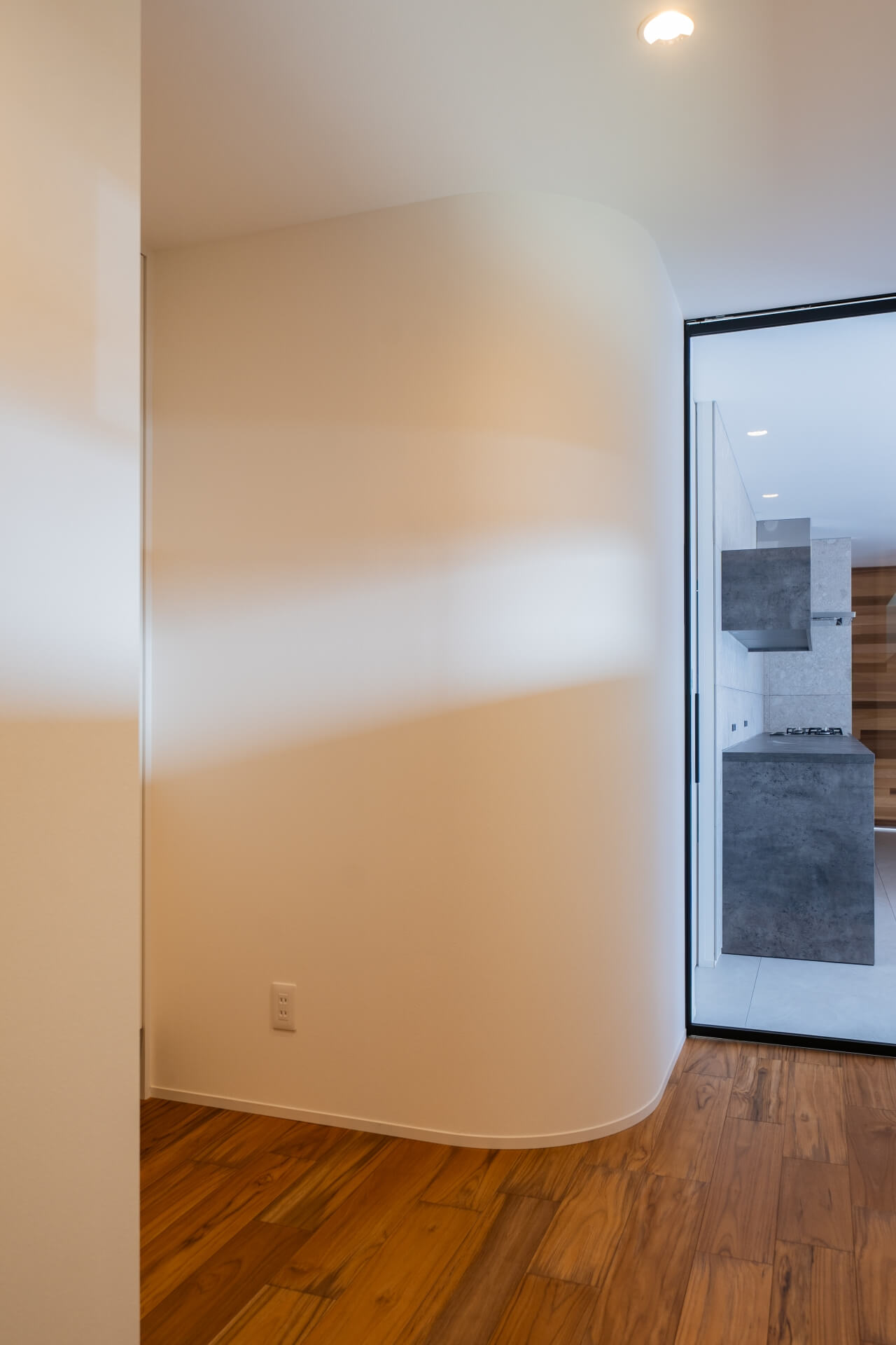 山梨県南アルプス市寺部の新築現場、曲面の壁越しにLDKへとつながる空間。奥にキッチンが見える玄関ホール。