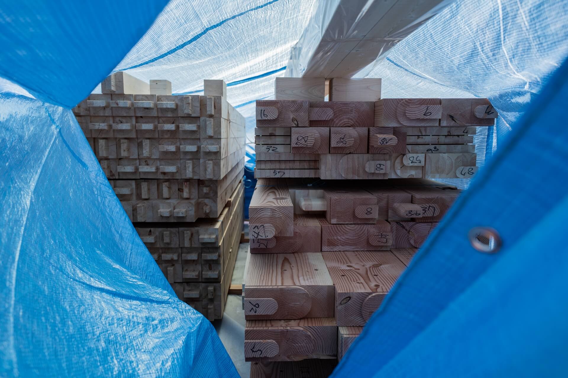 山梨県富士吉田市大明見の建築現場。ブルーシートの中に整然と積まれた構造材。加工された木材が上棟を待つ状態。