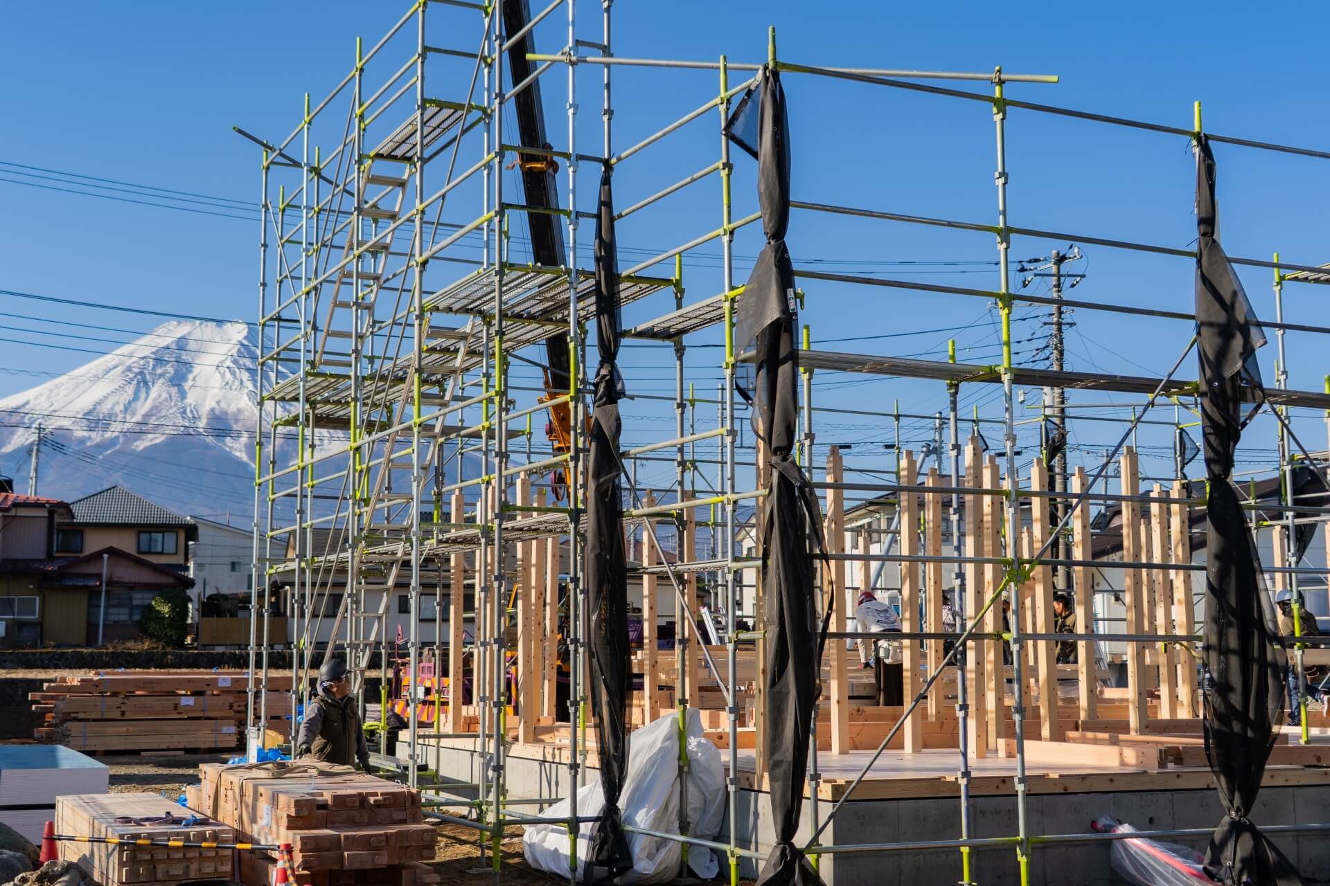 山梨県富士吉田市大明見の建築現場で富士山を背景に柱を建てている上棟作業。