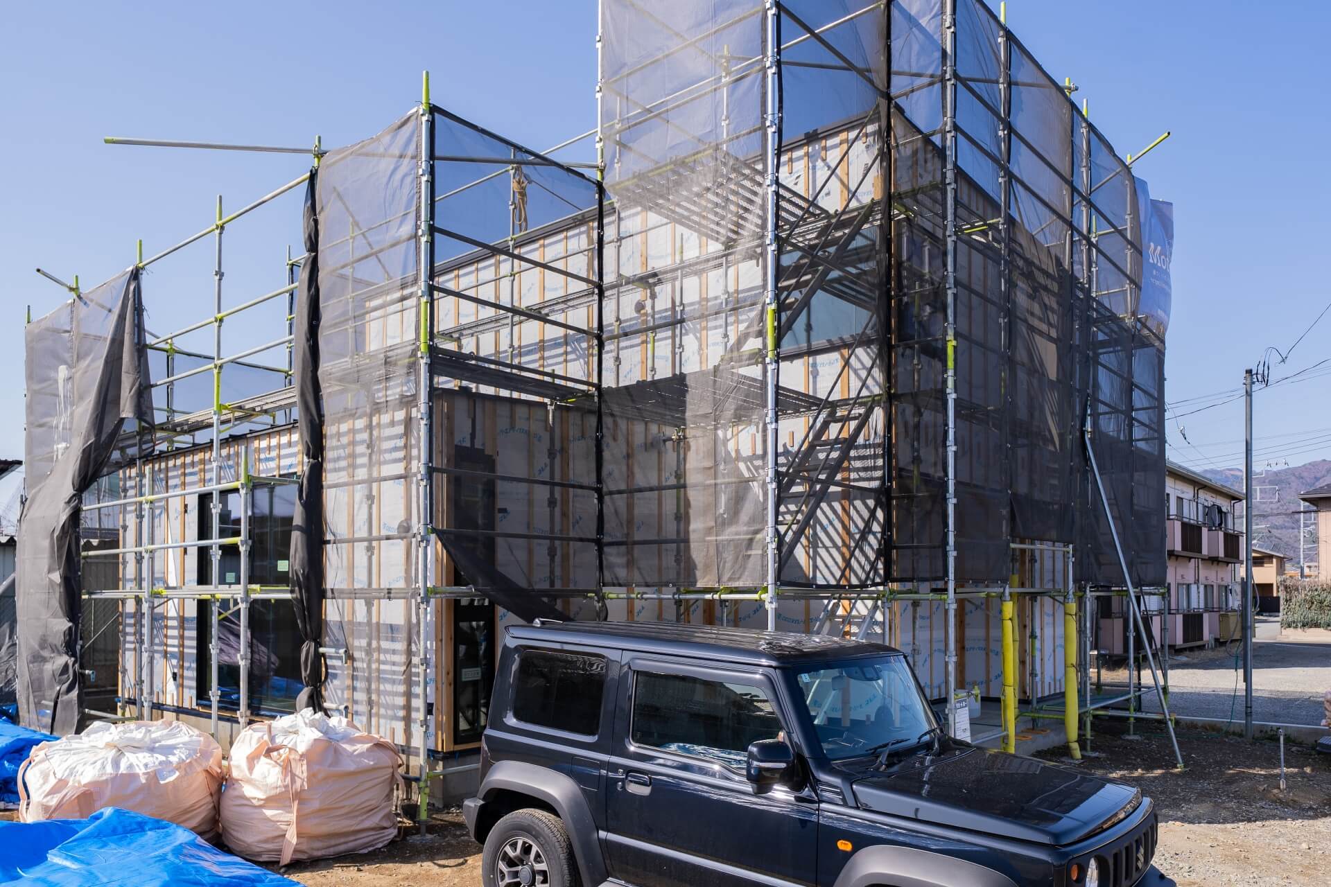 山梨県甲府市蓬沢の新築現場にて、足場と養生ネットに囲われた新築住宅の外観の様子。