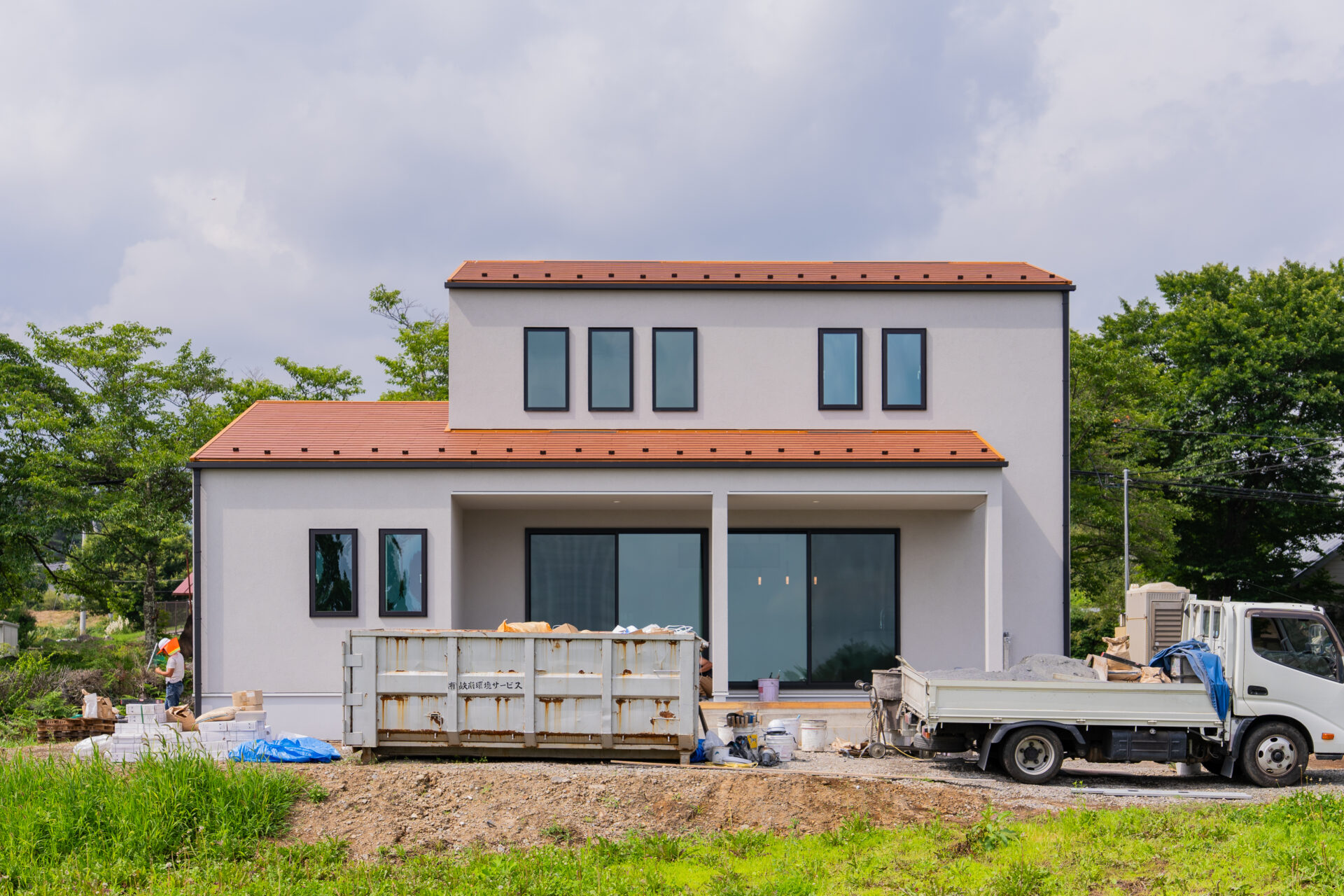 山梨県北杜市大泉町西井出の建築現場の足場が外れた外観の様子。オレンジの屋根と薄いグレーの壁に仕上がっている。