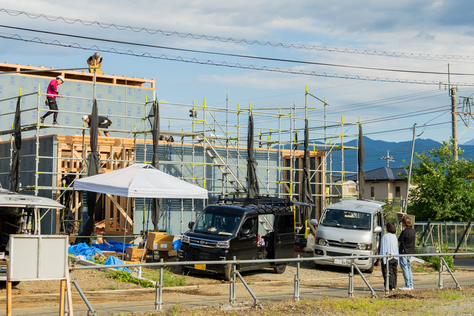 甲府市善光寺にて上棟作業が進む木造住宅を見守る施主様と建築現場。