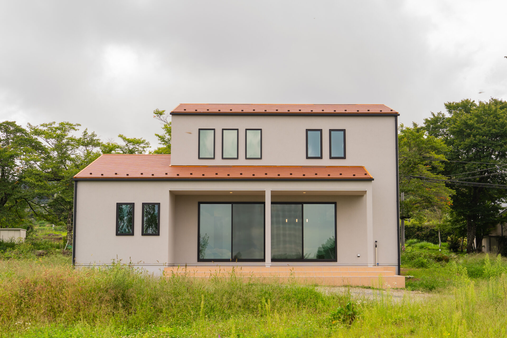 北杜市大泉町西井出の建築現場。切妻屋根と大きなテラスを備えたシンプルな外観の住まい。
