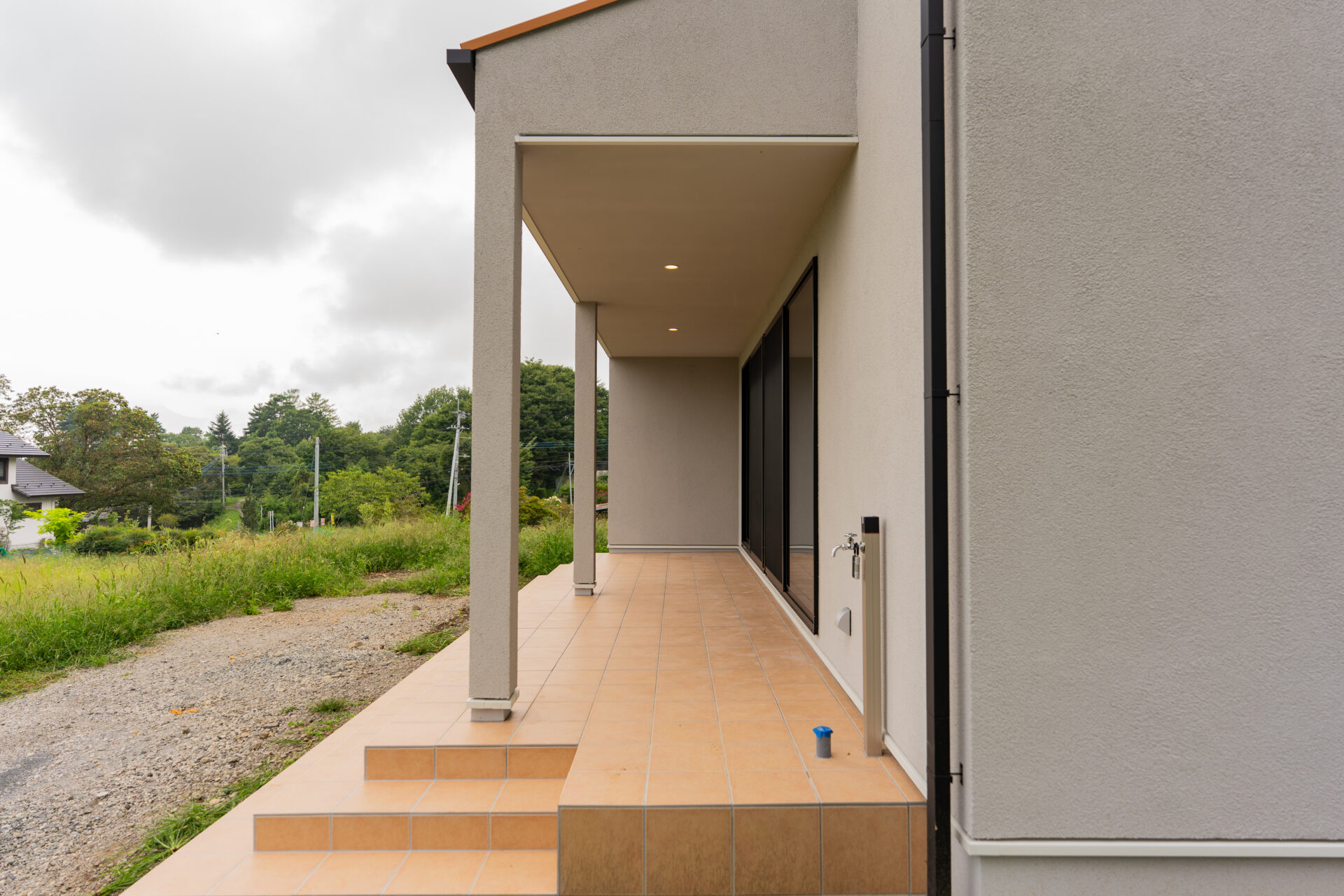 北杜市大泉町西井出の建築現場。奥行きのある屋根付きテラスと外部水栓のある外観側面。