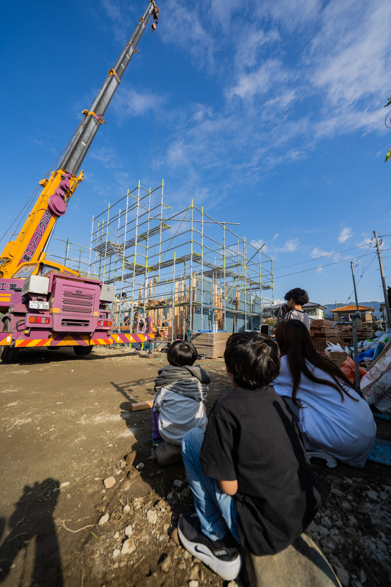 笛吹市石和町東高橋の新築工事。大工さんたちによる建て方作業と、その様子を見守るご家族を捉えた上棟当日の一枚。